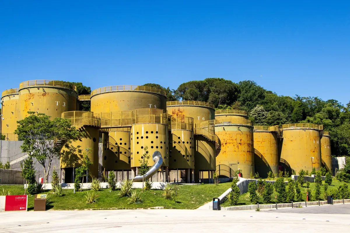 Series of large yellow industrial cylinders in a green park setting under a clear blue sky.